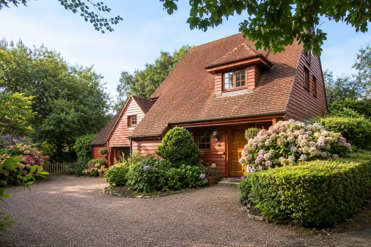 Brickmoor, a detached cottage-style house with tiled roof set among trees, hydrangeas and gardens near Yeoford, Devon